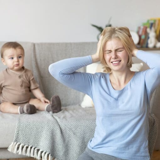 Stressed Mother Suffering From Headache, Sitting With Baby At Home