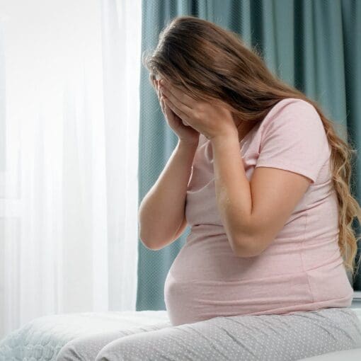 Sad Crying Pregnant Woman Suffering From Depression Sitting On Bed And Holding Her Head. Concept Of
